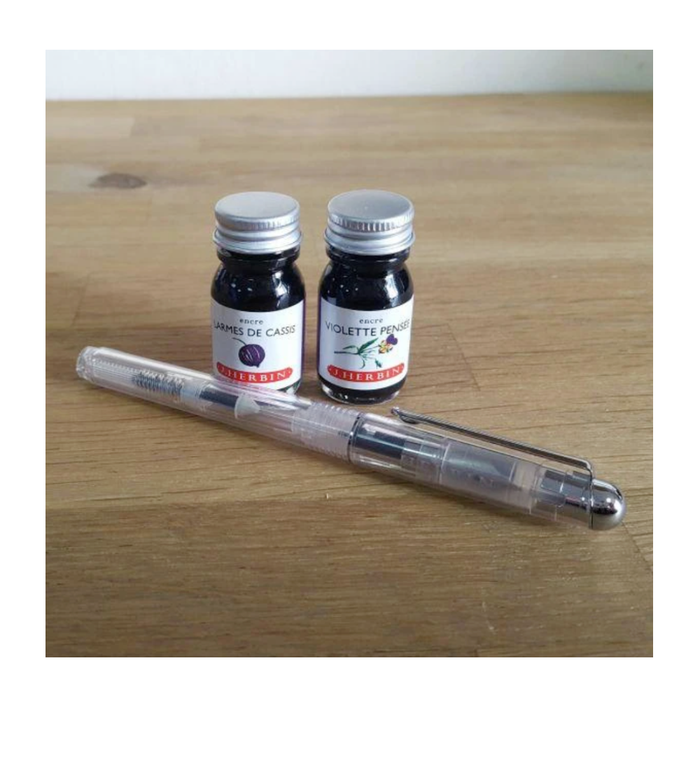 Jacques Herbin clear fountain pen on desk with bottled ink for writing